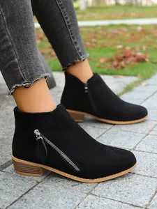 Close-up view of black suede ankle boots with dual side zippers on paved path outdoors