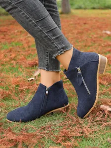Close-up view of navy blue suede women's ankle boots with dual zippers on autumn grass