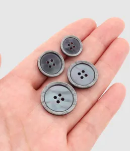 Four different sizes of grey pearl resin buttons held in palm for scale comparison.