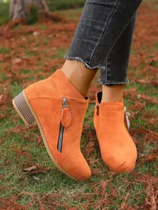 Close-up of stylish orange suede ankle boots with side zippers and pointed toe design