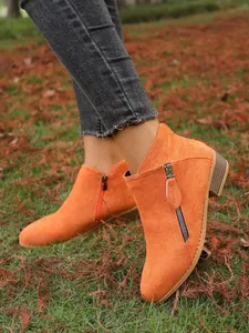 Detail view of stylish orange suede ankle boots with side zippers and chunky heels