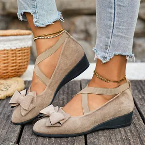 Dettaglio scarpe con zeppa in camoscio con fiocco e cinturini elastici incrociati.