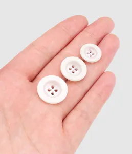 Close-up detail of three white resin four-hole buttons in different sizes held in hand