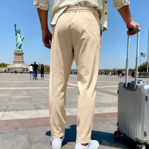 Man wearing beige knitted joggers with a silver suitcase near the Statue of Liberty