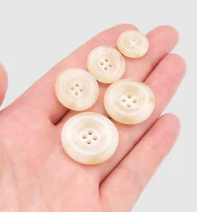 Detailed view of high-quality cream resin four-hole buttons in various sizes held in a palm