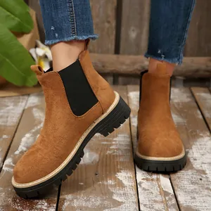 Detailed view of women's brown suede Chelsea boots featuring thick black soles on wooden floor.