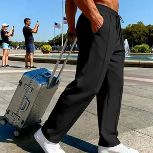 Schwarze Herren-Freizeithose im Reisekontext mit Koffer auf einem Platz im Freien gezeigt