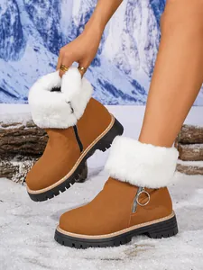 Close-up of brown suede snow boots with white faux fur trim in a snowy outdoor scene