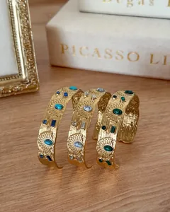Close-up detail of three gold stainless steel cuff bracelets with colorful stone inlays