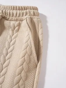 Dettaglio di joggers beige da uomo con maglia a trecce e trama trapuntata particolare.