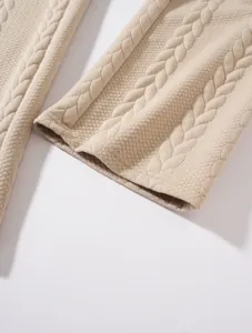 Primo piano dell'orlo dei pantaloni in maglia beige con dettaglio della trama a trecce.