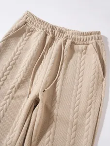 Vista macro di pantaloni sportivi beige in maglia a trecce con coulisse e texture morbida.