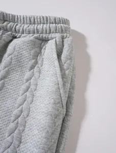 Primo piano dettagliato di pantaloni sportivi trapuntati grigi con vita e tasca laterale.