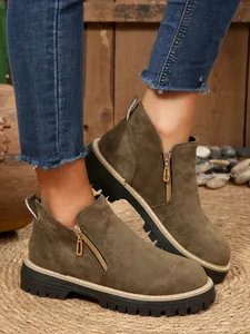 Détail de bottines en daim vert olive avec fermeture éclair dorée et semelle crantée