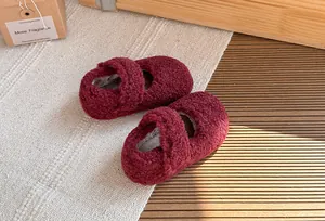 Dettaglio scarpe neonato in pile bordeaux su un accogliente tappeto bianco strutturato