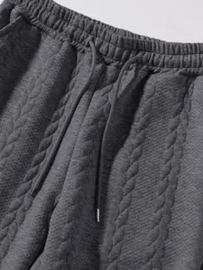 Dettaglio ravvicinato di pantaloni grigio scuro da uomo con coulisse e tessuto trapuntato.