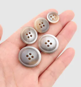 Vue détaillée de divers boutons en résine avec texture en corne tenus en main pour l'échelle