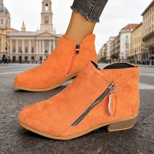 Detail of orange suede ankle boots showing dual side zippers and chunky heel design.