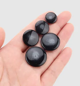 Lot de cinq boutons en résine noire brillante de tailles variées présentés sur une main