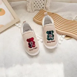 Close-up of children's canvas slip-on shoes featuring embroidered red and green bear motifs.