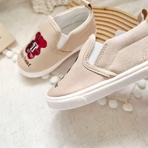 Close-up of beige children's canvas slip-ons with a cute cartoon bear embroidery.