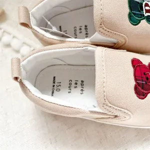 Detail of children's beige canvas slip-ons with cute bear embroidery