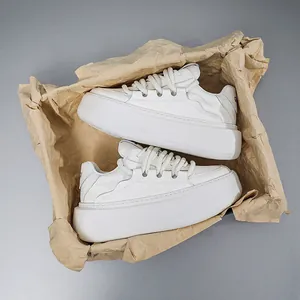 Detailed macro view of white chunky platform sneakers inside a crumpled kraft paper bag