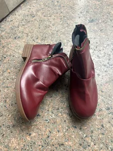Close-up detail of burgundy faux leather ankle boots with double side zippers on stone floor