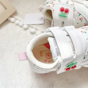 Close-up detail of white toddler walking shoes with cherry pattern and Velcro strap