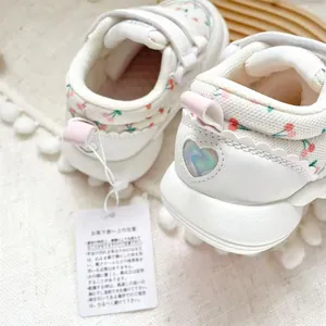 Close-up of white baby walking shoes with cherry patterns and heart-shaped heel detail