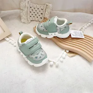 Close-up of sage green toddler sneakers with dinosaur patterns and velcro straps