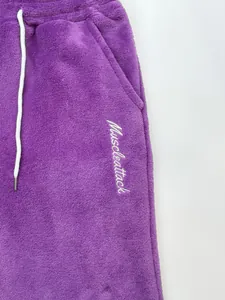 Close-up of soft purple coral fleece joggers with white muscleattack embroidery detail