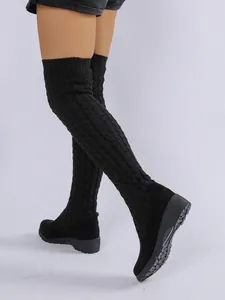 Vista detallada de botas altas de cuña con punto trenzado negro sobre la rodilla