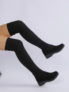 Vista detallada de botas altas de punto negro con tacón de cuña y diseño entrelazado