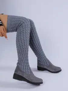 Vista detallada de botas grises por encima de la rodilla con punto trenzado y cuña alta.