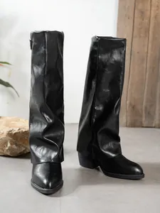 Close-up of black pointed-toe pant-leg boots with chunky heels and faux leather finish