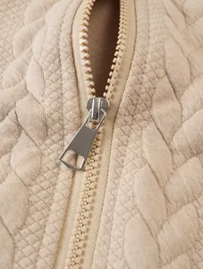 Detailed macro shot of a silver metal zipper on beige jacquard quilted sweatshirt fabric