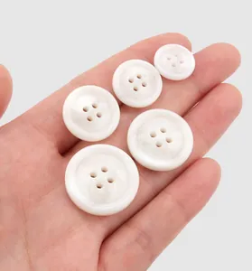 Close-up of white pearlescent resin four-hole buttons held in hand for scale