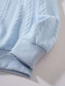 Close-up of light blue cable knit sweatshirt fabric showing texture and ribbed cuff.