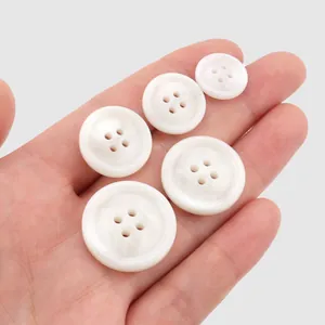Five white resin four-hole buttons held in hand for scale comparison