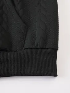 Detail shot of black men's sweatshirt showing quilted jacquard texture and ribbed hem
