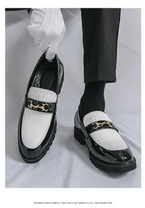 Détail de mocassins en cuir noir et blanc pour homme avec mors doré et texture croco.