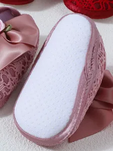 Detailed close-up of pink baby lace shoes showing the white anti-slip dotted sole design