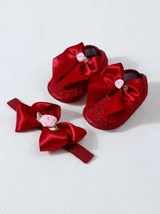 Close-up of red lace baby shoes and matching bow headband with elegant pink rose detail.