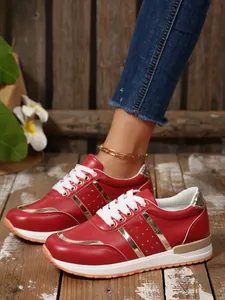 Dettaglio di scarpe da ginnastica rosse da donna con strisce dorate su pavimento in legno