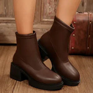 Detalle de botines Chelsea marrones con punta redonda y tacón en suelo de madera