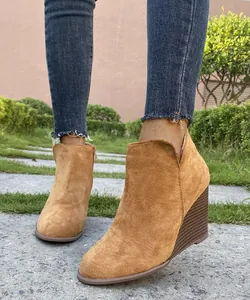 Detail view of stylish tan suede wedge ankle boots paired with frayed blue denim jeans.
