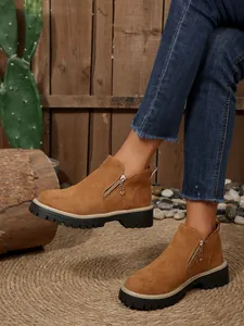 Détail de bottines marron en daim avec zip latéral et semelles crantées noires.
