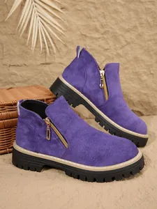 Gros plan de bottines en daim violet avec fermeture éclair latérale dorée et semelle épaisse