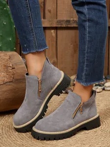 Gros plan sur des bottines grises en daim à bout rond avec zip doré et semelle épaisse à crampons